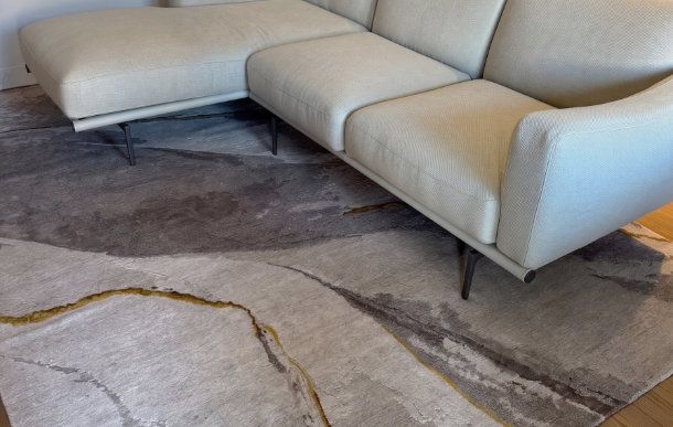 Sezione di un divano componibile moderno grigio chiaro posizionata su un tappeto contemporaneo con design astratto e sottili linee dorate.